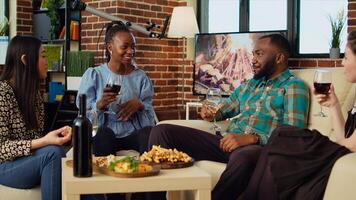 Diverse mates having engaging conversation during apartment party in cozy house. Happy group of people talking in living room, eating snacks and drinking alcoholic beverages photo