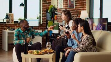 multirracial grupo de amigos hablando con cada otro en elegante departamento, reunido juntos a celebrar día festivo. multiétnico colegas socializando a hogar, disfrutando alcohólico bebidas foto