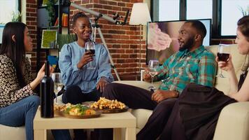 African american woman captivating friends at apartment party with compelling story. Guest making multiracial group of people laugh in stylish living room while drinking and eating photo