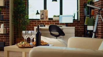 Panning shot of empty cozy apartment living room with appetizer platter and wine bottle on wooden table, awaiting guests to arrive. House interior with leather couch and TV running in background photo