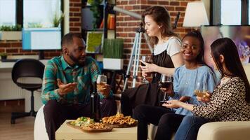 Diverse group friends celebrating asian woman birthday, drinking alcoholic beverages and eating gourmet cheese. Cheerful guests laughing in brick wall living room after gifting host presents photo