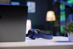 Selective focus on wireless headphones placed on a table near digital laptop. Image showing electronic devices kept on a desk for an individual to use. photo