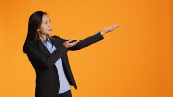 Asian office worker points to both sides of the background, creating new web promotional ad in orange studio. Young businesswoman working on marketing advertisement during shoot. photo