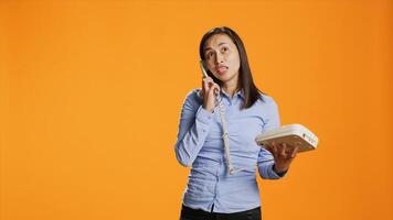 As she chats on retro line, asian woman conducts remote call on her landline phone. Satisfied female model picks up cable office phone and engaging distantly in front of camera. photo