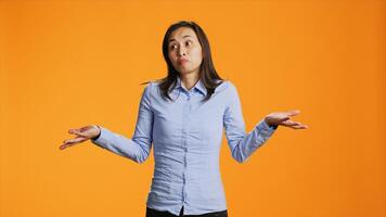 Doubtful model raising shoulders over orange background, showing doubt and being clueless about answer. Young filipino person acting uncertain and confused standing in front of camera. photo