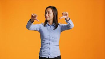 Asian person giving thumbs down in front of studio camera, expressing negativity and disapproval with dislike symbol. Negative woman showing rejection, being upset and displeased. photo