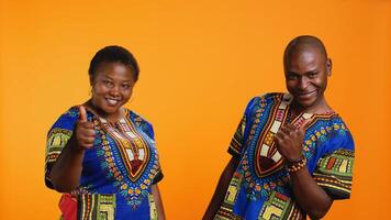 African american couple showing thumbs up symbol on camera, feeling positive and presenting their satisfaction. Married people expressing approval and giving like sign in studio. photo