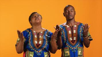 Ethnic couple praying to God with arms spread on camera, showing belief in spirituality and religion. African american people asking for a miracle, begging for good luck and fortune in studio. photo