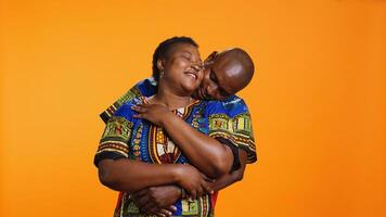 Sweet african american couple embracing in studio, holding each other and expressing their sincere feelings. Ethnic romantic man hugging his wife on camera over orange background. photo