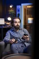 Man holding remote control while watching interesting movie on streaming service, enjoying time off from work. Person on couch surprised by high quality film broadcasted on TV photo