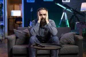 Man gasping while watching horror movie on streaming service, enjoying time off from work. Person covering mouth in disbelief, surprised by film scene broadcasted on TV set photo