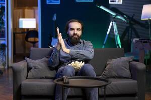 Man rubbing hand in anticipation, eager to watch shows on TV, eating popcorn, paying close attention to screen. Impatient man sitting on couch in apartment, aching to catch favorite television series photo