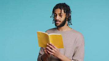 Middle Eastern man reading book from publisher aloud, telling story, enjoying hobby. BIPOC person narrating literature novel, doing critique essay, isolated over studio background, camera B photo