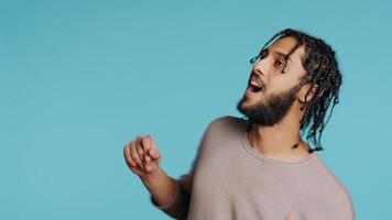 Happy Middle Eastern dancer having fun, dancing on rhythm, enjoying leisure time. Cheerful BIPOC man entertaining himself doing funky movements on music, studio background, camera B close up photo