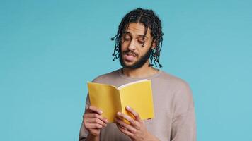 Middle Eastern man reading newly released hardcover book from publisher, entertained by engrossing story. BIPOC person enjoying literature novel during leisure time in studio background, camera B photo