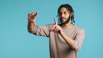 Happy person using augmented reality technology, doing swiping motions. BIPOC man using futuristic AR tech, making pinching zooming gesturing, blue studio background, camera A photo