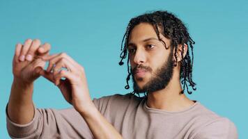Happy person using augmented reality technology, doing swiping motions. BIPOC man using futuristic AR tech, making pinching zooming gesturing, blue studio background, camera B close up photo