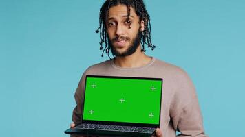 Joyous BIPOC man holding green screen laptop, having positive mood. Smiling person presenting chroma key notebook, doing recommendation, isolated over studio background, camera B photo