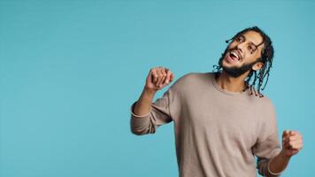 Happy Middle Eastern dancer having fun, dancing on rhythm, enjoying leisure time. Cheerful BIPOC man entertaining himself doing funky movements on music, studio background, camera A photo