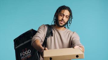 Portrait of BIPOC courier delivering pizza order to client. Delivery part time worker using thermal backpack to store food and bring it to customer, isolated over studio background, camera A photo