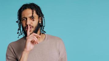 Annoyed Middle Eastern man doing shushing hand gesturing, irritated by noise, having negative mood. Assertive person placing finger on lips, doing quiet sign gesture, studio background, camera B photo