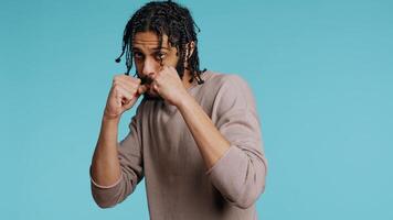 Middle Eastern man pretending to fight, throwing punches, holding defensive guard. BIPOC martial artist person mock boxing, holding combat stance, exercising in blue studio background, camera B photo