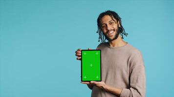 Joyful man holding green screen tablet, showing positive emotion. Upbeat person presenting chroma key device, doing recommendation, isolated over studio background, camera A photo