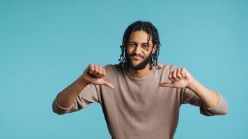 Upset Middle Eastern man showing thumbs down sign gesturing, disapproving, offering negative feedback. Disappointed BIPOC person doing rejection hand gesture, studio background, camera A photo