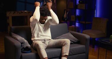 Gamer upset after receiving game over screen while fighting enemies, throwing controller in frustration. African american man sad after losing videogame on console system photo