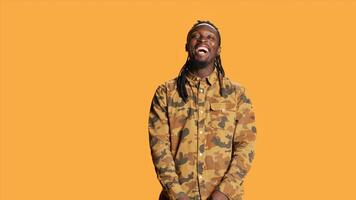 Joyful person enjoying studio shoot and laughing, making jokes on camera and acting playful. Silly funny african american man having fun over orange background, relaxed cool guy. photo