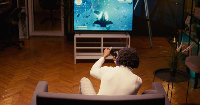 Gamer shooting foes, trying to defeat them in classic arcade space shooter videogame on smart TV. Man spamming buttons on controller to complete missions in singleplayer game photo