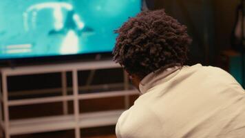 Man in living room using cloud gaming service to play demanding science fiction videogame on TV. Player enjoying high quality ray tracing graphics, streaming game over the internet, close up shot photo