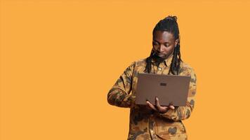 African american guy looks at information on laptop, searching for something on online webpages using portable computer. Young person in studio holding pc and looking at network sites. photo