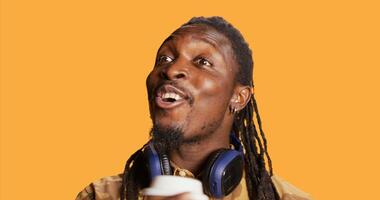 Cheerful guy serving hot cup of coffee in studio, enjoying beverage to gain more energy. African american smiling man drinking caffeine beverage on camera, feeling relaxed and pleased. photo