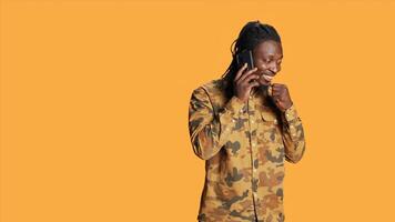 Young person answering phone call on camera, talking to friends on remote telephone line over orange background. African american man enjoying telecommunication conversation. photo