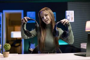 Cheerful gen Z influencer in studio films headphones comparison video review for audience. Upbeat girl hosts technology online show, unboxing music listening devices for her fanbase photo