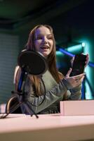 Teenager content creator filming technology review of newly released smartphone, unpacking it and presenting specifications to audience. Media star showing cellphone to fans from studio photo