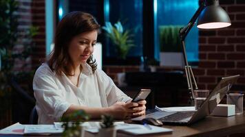 Smiling manager looking at text messages on smartphone, taking break from working on company project. Team leader unwinding by using phone to browse social media in office, camera B photo