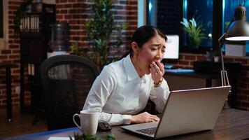 Tired employee asleep on computer desk chair suddenly waking up, struggling to finish writing emails. Drowsy businesswoman working overnight, typing on laptop, trying to stay awake, camera A photo