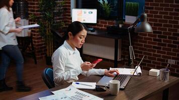 Stressed businesswoman doing multitasking, answering phone while crosschecking data between laptop and paperwork. Worker taking telephone call and comparing financial statistical graphs photo