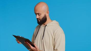 Middle eastern adult creating a checklist on clipboard papers, being focused on trying to plan tasks on an organizer in studio. Modern person looking at files and listing things to do. Camera 2. photo