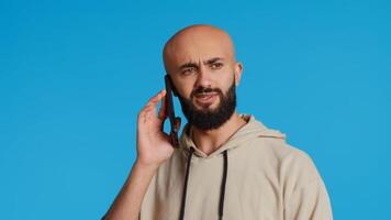 Middle eastern guy chatting with friends on phone call, answering smartphone while standing over blue background. Modern man discussing something on a remote network. Camera 2. Handheld shot. photo