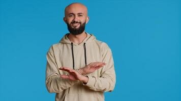 Arab male model doing no symbol on blue backdrop, showing his rejection and denial in studio. Middle eastern guy expressing refusal with a negative gesture, serious man. Camera 1. photo
