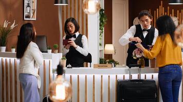 Tourists going through check in process at hotel reception desk, staff verifying passport id for registration. Two women signing ledger and reservation papers for accommodation on trip. photo