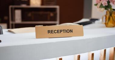 Reception sign placed on front desk in hotel lobby indicating place to book rooms and do check in process for accommodation. Empty resort hallway used to greet customers. Close up. photo