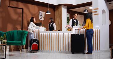 Asian guests approach reception to ask about accommodation, arriving at hotel and hoping for an early check in. Front desk staff team welcoming women and offering their services. Tripod shot. photo