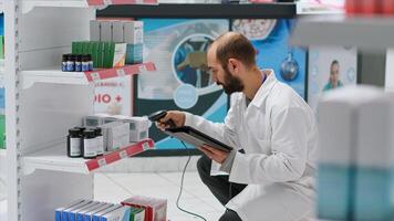 Pharmaceutical helper monitors the medication stock on shelves, scanning boxes that include prescribed medicine and cures at the clinic. Worker records medical supplies using tablet and scanner. photo