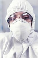 microbiólogo sentado en laboratorio vistiendo ppe mirando a cámara en moderno equipado laboratorio. cansado mujer científico en biotecnología laboratorio vistiendo protector traje durante global epidemia. foto