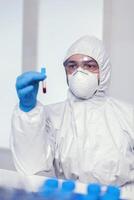 Biochemist in ppe suit looking and working with blood in test tube. Doctor working with various bacteria and tissue, pharmaceutical research for antibiotics against covid19. photo