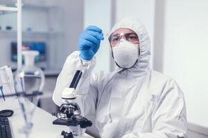 Medical scientist holding a microscope glass slide dressed in ppe during covid19. Examining vaccine evolution using high tech for researching treatment against covid19 virus. photo